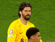 a man with a beard wearing a yellow nike jersey stands on a soccer field