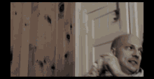 a bald man is talking on a cell phone in front of a wooden door