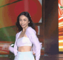 a woman in a white crop top and a pink jacket is standing on a stage .