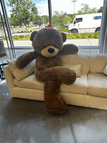 a large teddy bear is sitting on a white couch in front of a window