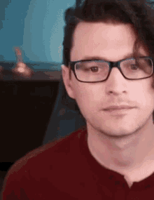 a man wearing glasses and a red shirt has a serious look on his face