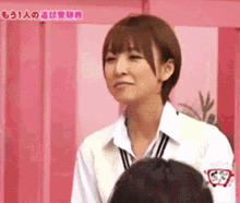 a woman in a white shirt is standing in front of a pink wall with chinese writing on it ..