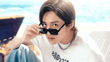 a young man is wearing sunglasses and a necklace while sitting on the beach .