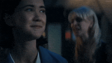 two women are standing next to each other in a dark room and talking .
