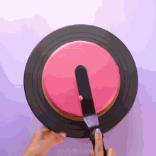 a person is using a spatula to spread pink frosting on a cake on a black plate