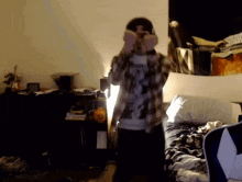 a man in a plaid shirt is covering his eyes in a bedroom