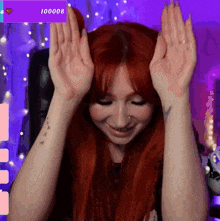 a woman with red hair holds her hands up in front of a purple screen that says ' 100000 ' on it