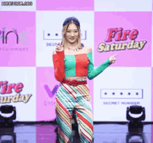 a woman is standing in front of a pink and white background that says fire saturday .