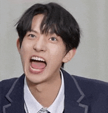 a young man in a suit and tie is making a funny face with his mouth wide open .