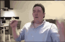 a man in a blue shirt is sitting in a living room holding something in his hands .