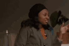 a woman wearing a beret and a sweater is sitting at a table with her hands in the air .