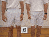 two men wearing white shorts are standing next to each other in front of a wall