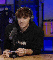 a man wearing headphones and a supreme hoodie is holding a pen in front of a microphone