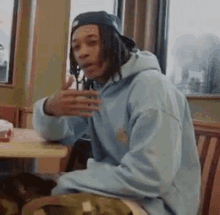 a man wearing a blue hoodie and a baseball cap is sitting at a table .