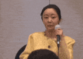 a woman in a yellow jacket is holding a microphone and speaking into it