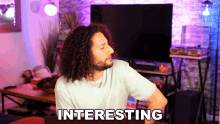a man with curly hair is sitting in front of a tv and the word interesting is on the screen