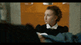 a woman in a black shirt and white collar is looking at herself in a mirror