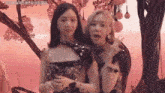 a couple of women standing next to each other in front of a pink background .