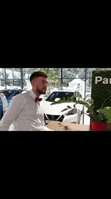 a man wearing a bow tie is standing in front of a car in a car dealership .