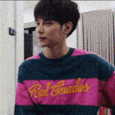 a young man wearing a pink and blue striped sweater with the word red grades on it .