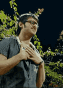 a man wearing glasses is holding his hands to his chest