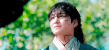 a young man with blood on his neck is standing in front of a tree .