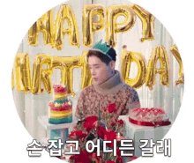 a man is sitting at a table with a birthday cake and balloons .