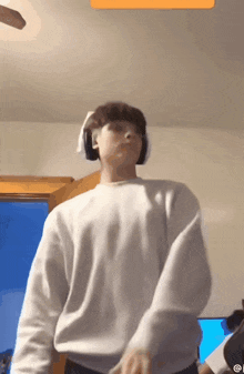 a man wearing headphones and a white sweater is dancing in a room