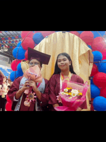 two female graduates are holding bouquets of flowers