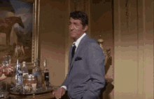 a man in a suit and tie is standing in front of a table with bottles of alcohol on it