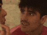 a man with a mustache is touching another man 's face .
