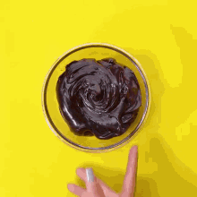 a person 's hand is reaching into a bowl of chocolate spread on a yellow background .
