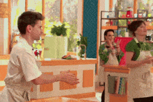 a man in an apron is clapping in front of a woman in a green shirt