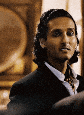 a man with long hair is wearing a suit and tie and looking at the camera .