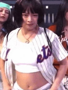 a woman is wearing a baseball jersey and a crop top while dancing .