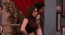 a man and a woman are standing next to each other in a room with a red curtain .