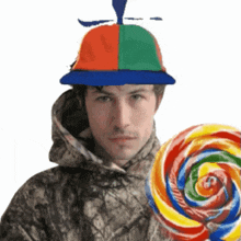 a man wearing a colorful hat is holding a large lollipop