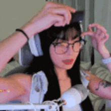 a woman wearing glasses and headphones is sitting in a chair and adjusting her hair .