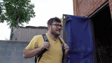 a man wearing glasses and a yellow shirt is carrying a black backpack