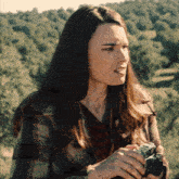 a woman in a plaid coat holds a camera in her hands