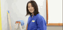a woman in a blue jacket is standing next to a wooden ladder and smiling .