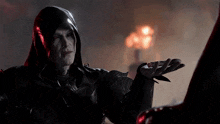 a man in a black hooded costume holds out his hand