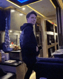 a young man in a black hoodie is standing in a kitchen