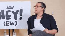 a man is sitting in front of a sign that says hey ( ew )