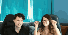 a man and woman are sitting on a couch with their arms in the air