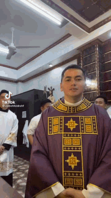 a priest is standing in a church wearing a purple robe with a gold cross on it .