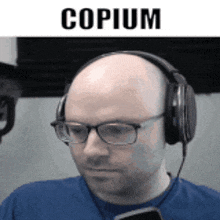 a bald man wearing headphones and glasses is looking at a cell phone .