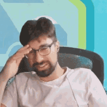 a man with glasses and a beard is saluting while sitting in a chair .