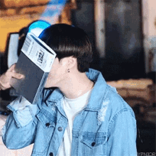 a man in a denim jacket is covering his face with a book