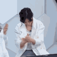 a woman in a white jacket is clapping her hands while another woman looks on .